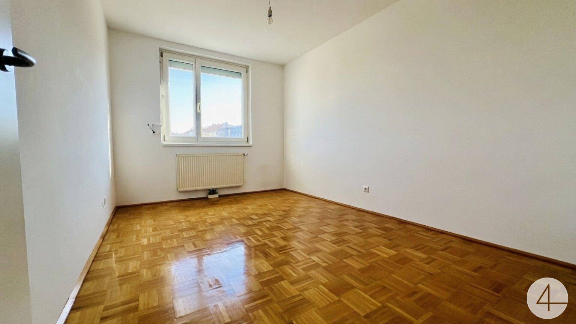 Helles Schlafzimmer mit Parkettboden, weißen Wänden und großem Fenster.
