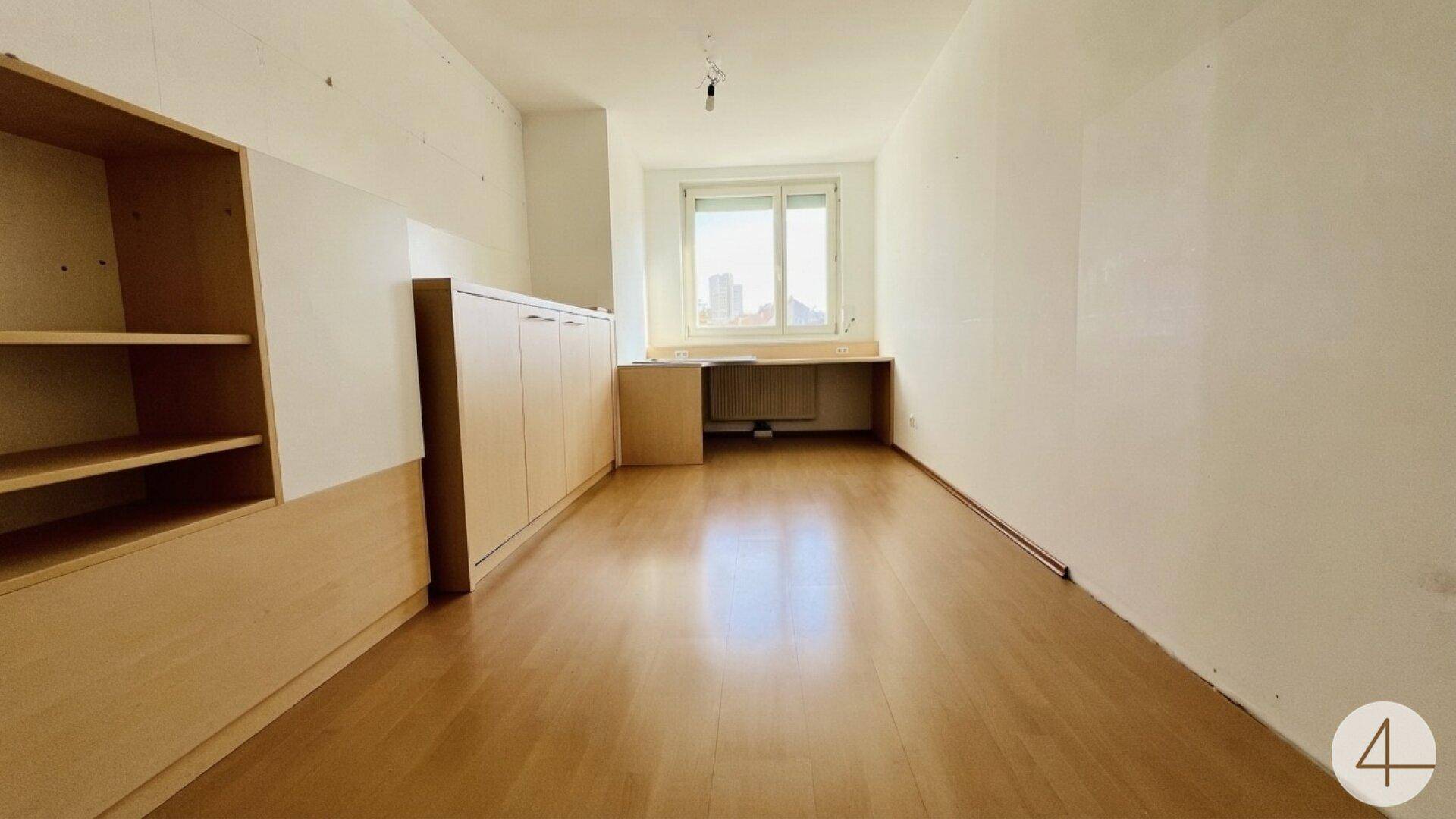 Geräumiges Zimmer mit Laminatboden, Einbauschränken und Arbeitsbereich am Fenster.
