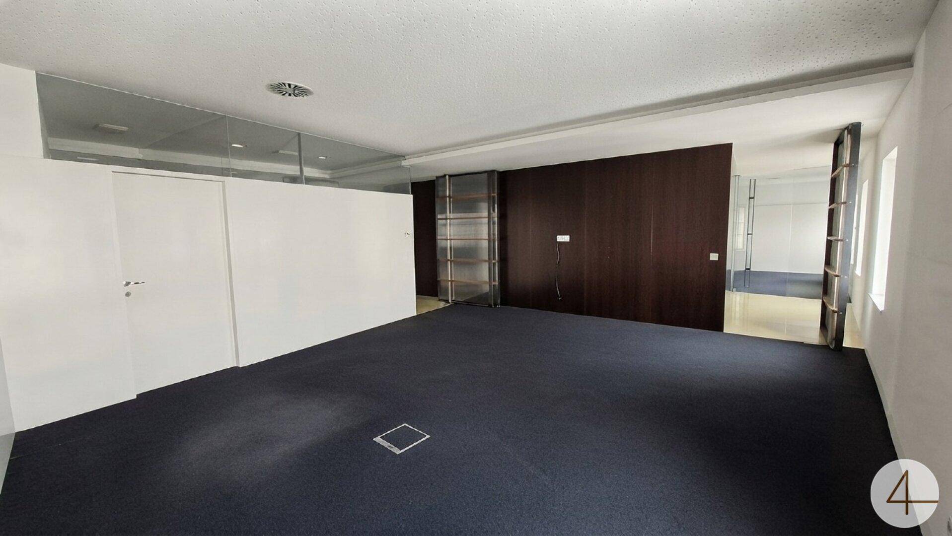 Offener Bürobereich mit dunklem Teppichboden, Holzwand und Glasabtrennungen.