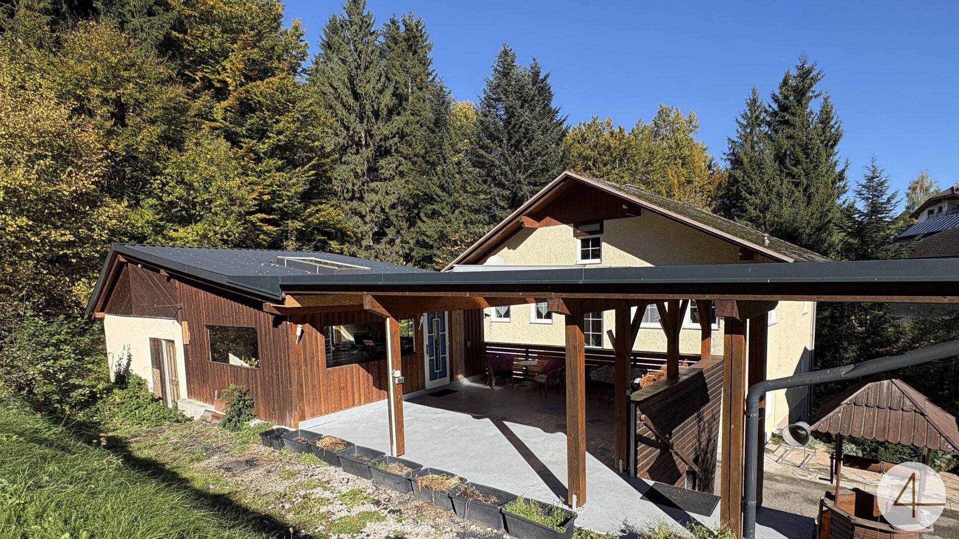 Ansicht des Hauses mit einem überdachten Eingangsbereich und Carport, umgeben von Bäumen.
