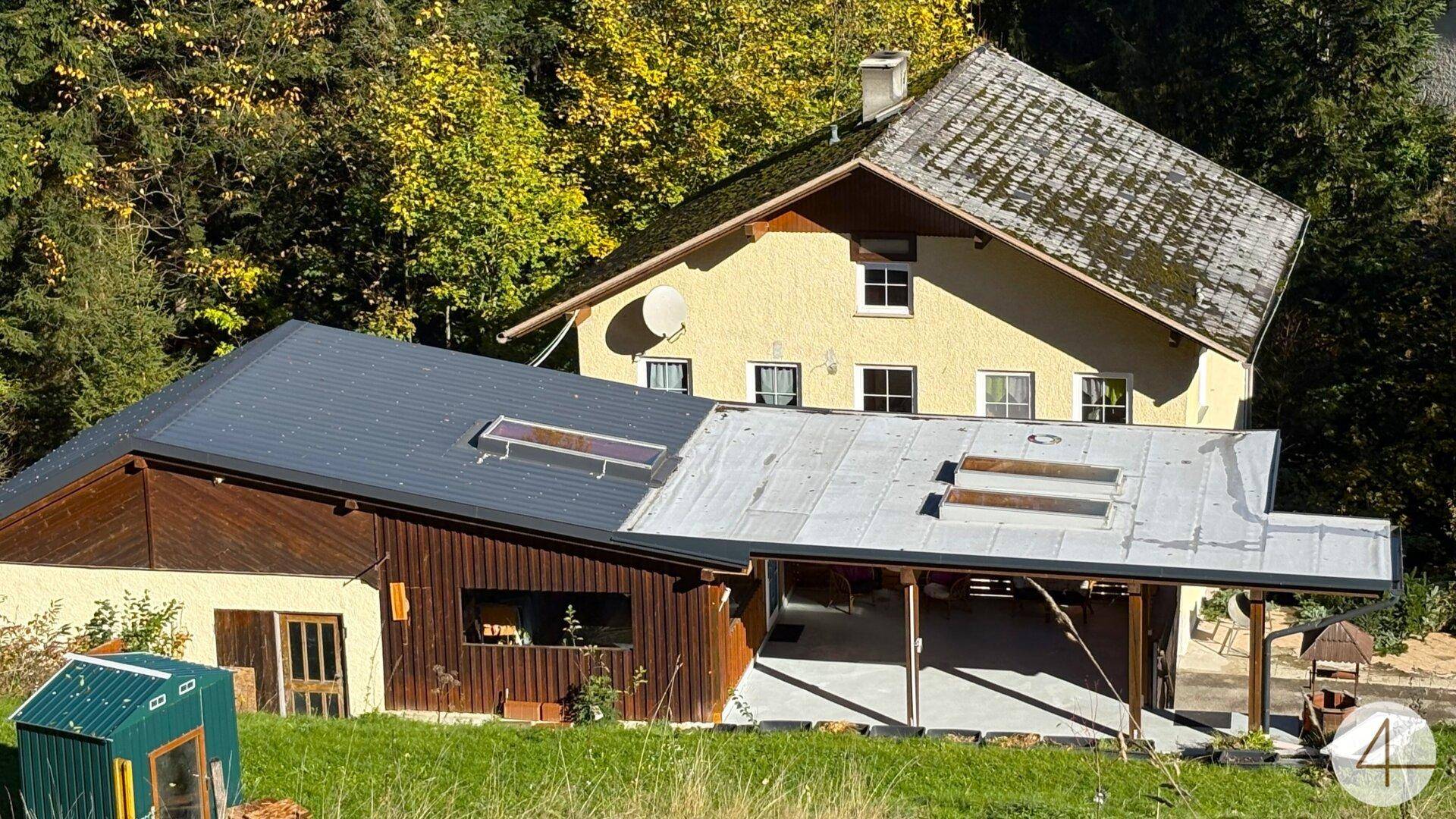 Nahaufnahme der beiden Gebäude mit unterschiedlichen Dächern, eingebettet in eine grüne Hügellandschaft.