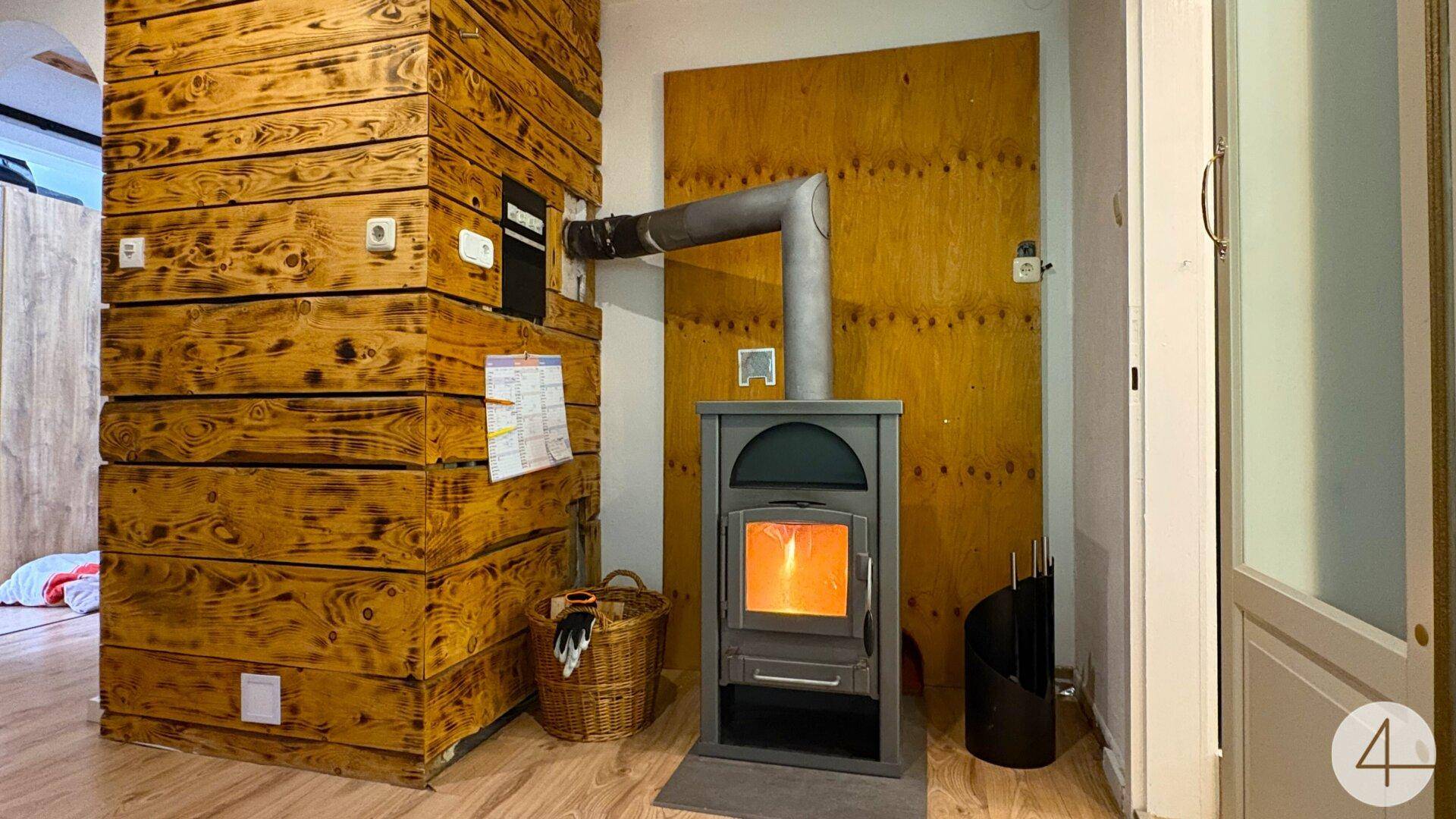 Innenraum mit einem modernen Holzofen und einer Holzwandverkleidung, die Wärme spendet.