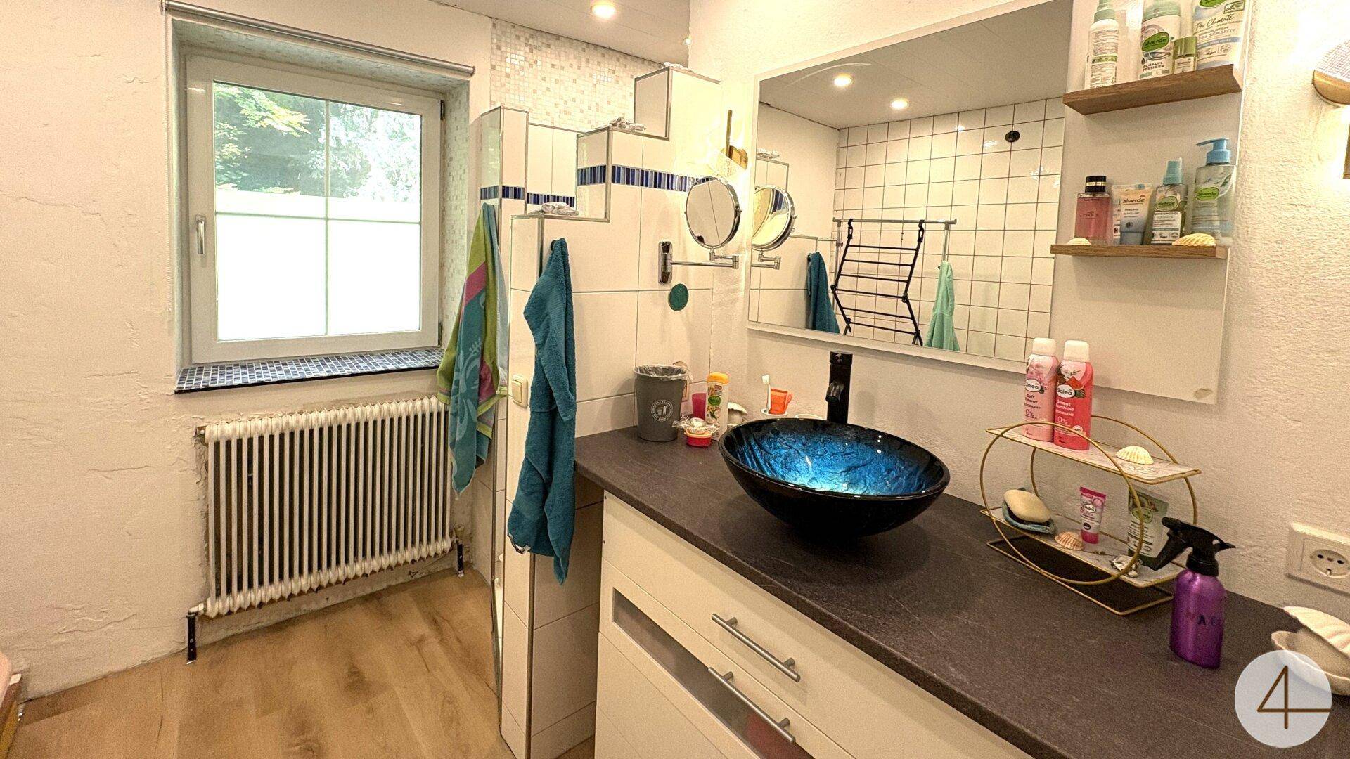 Modernes Badezimmer mit blauem Waschbecken, großem Spiegel und Fenster für natürliches Licht.