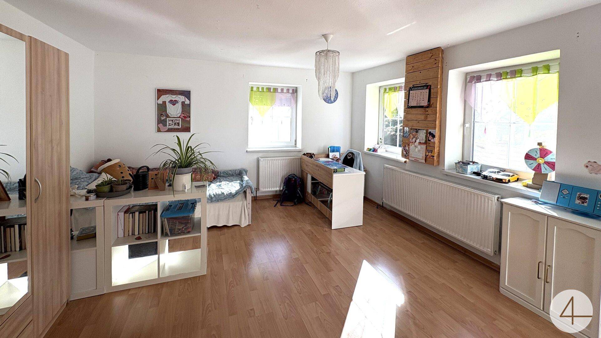 Helles Schlafzimmer mit Holzfußboden, großen Fenstern und einfacher, funktionaler Einrichtung.