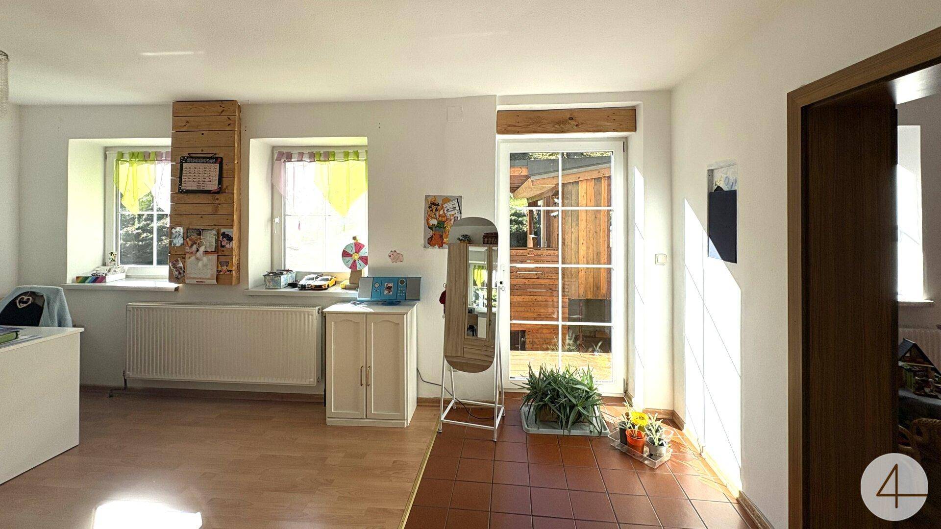 Heller Wohnbereich mit Zugang nach draußen, Holzfußboden und großen Fenstern.