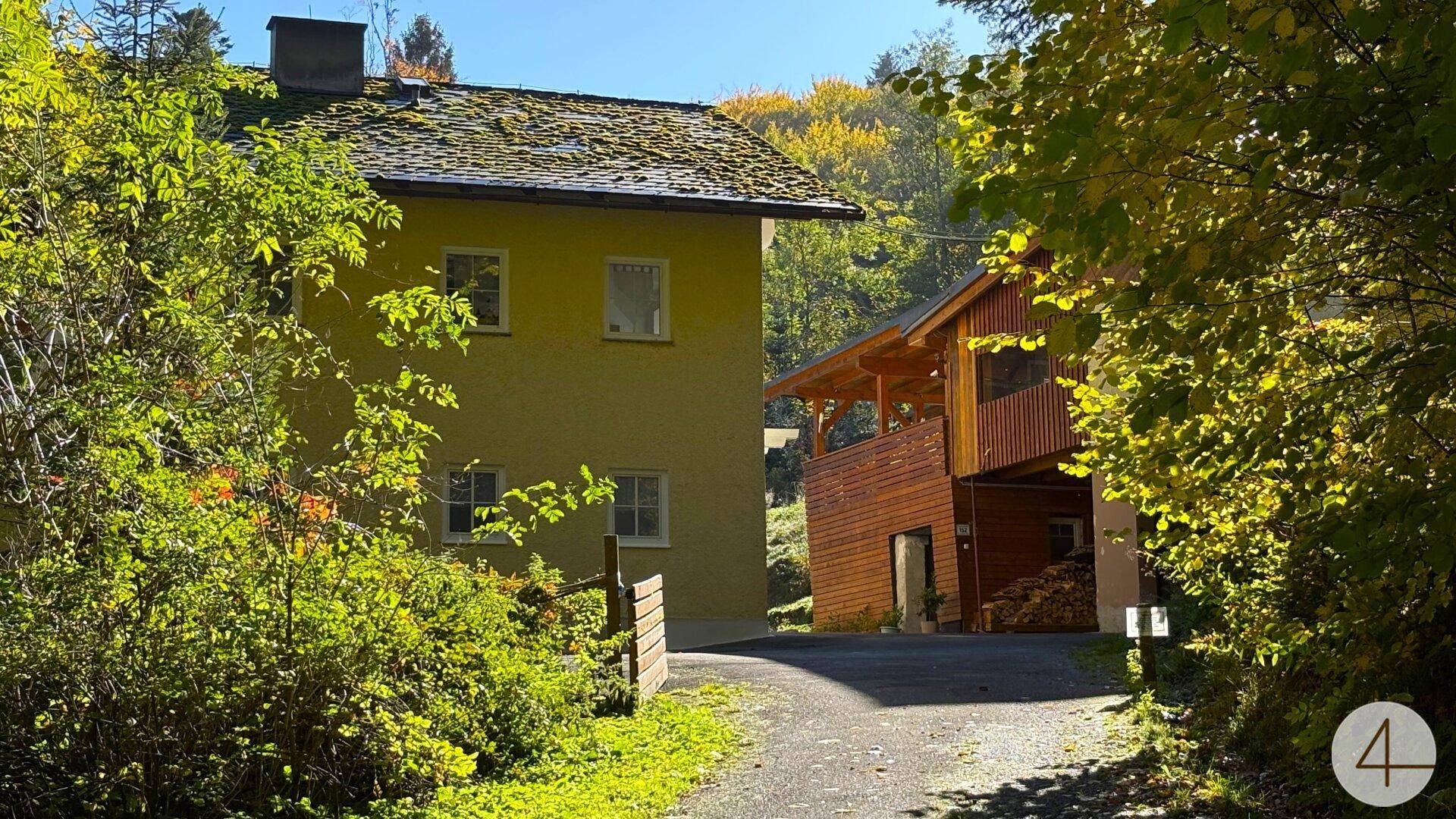 Zwei Gebäude, umgeben von dichtem Grün und Bäumen, mit einem Weg im Vordergrund.