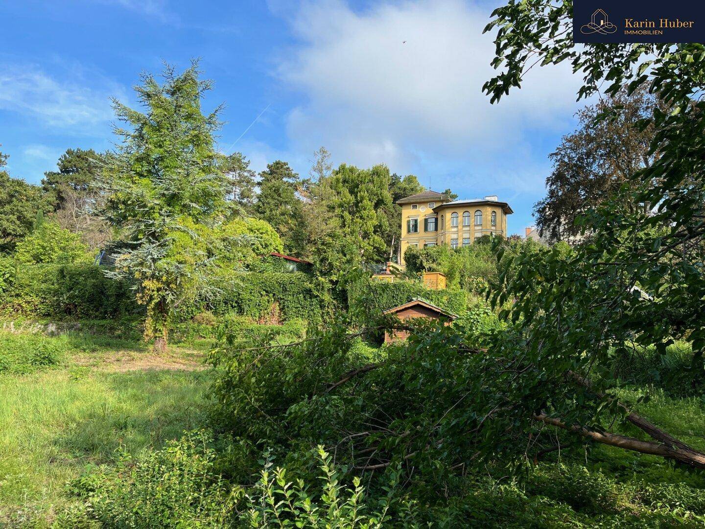 Blick auf eine historische Villa auf einem Hügel, umgeben von üppigem Grün und Bäumen.