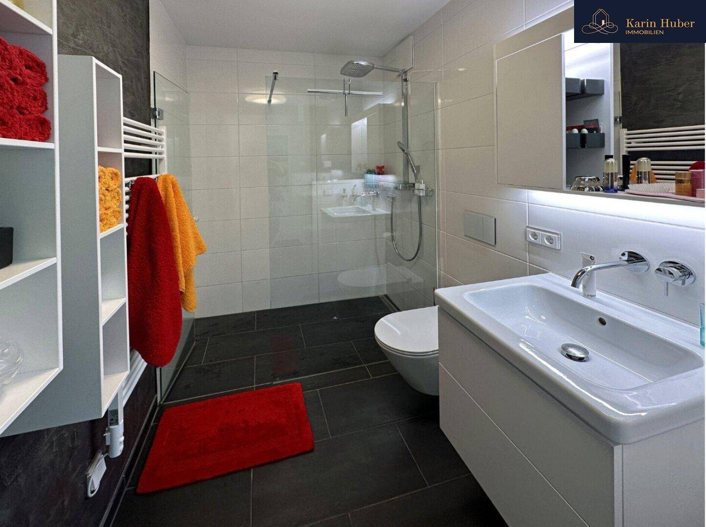 Modernes Badezimmer mit begehbarer Dusche, Wand-WC und eleganten dunklen Bodenfliesen.