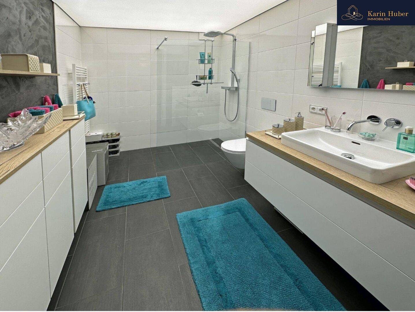 Geräumiges Badezimmer mit großer begehbarer Dusche, modernem Waschtisch und dunklen Bodenfliesen.