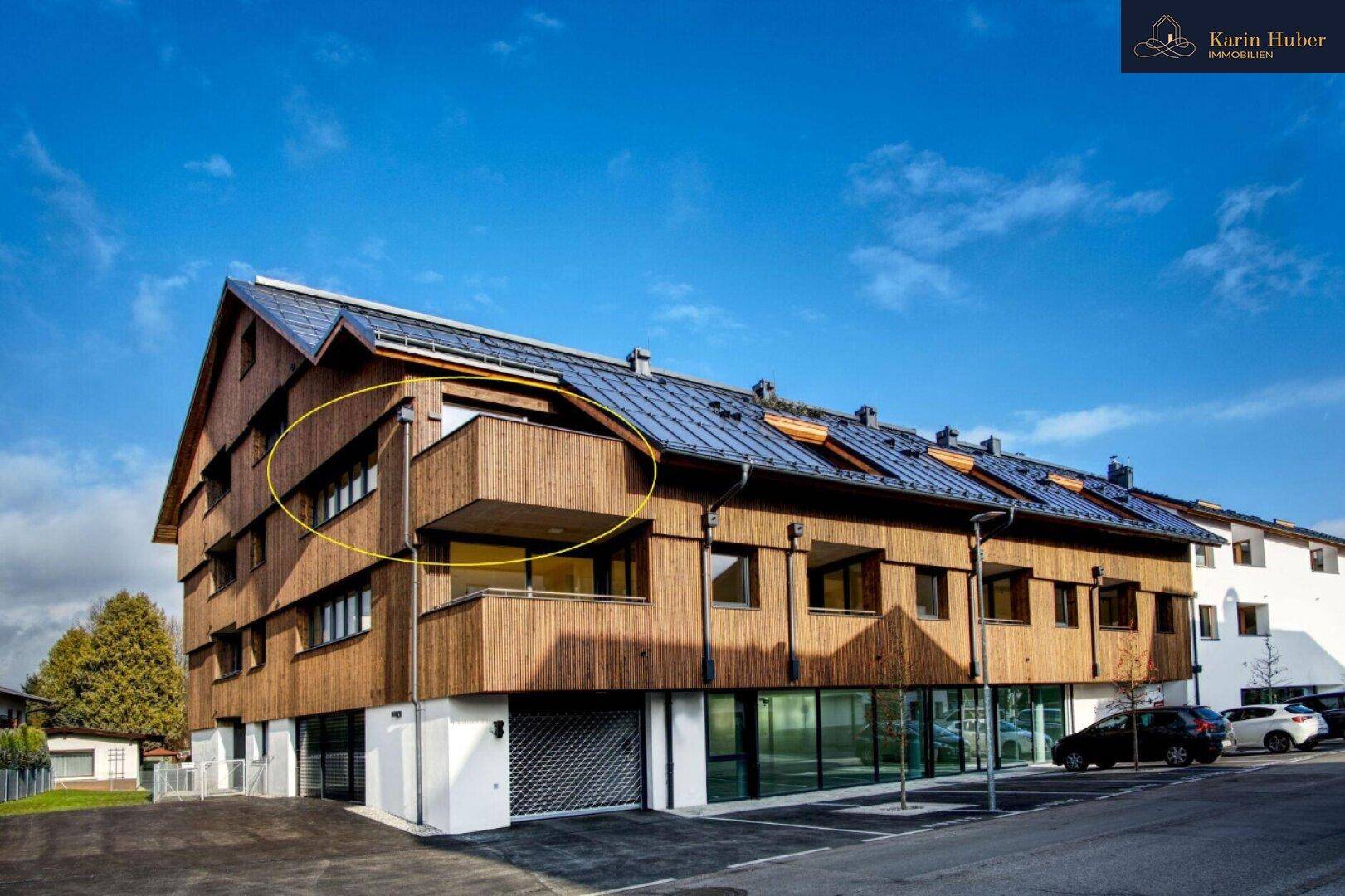 Moderne Holzfassade eines Mehrfamilienhauses mit Balkonen und großen Fenstern unter blauem Himmel.