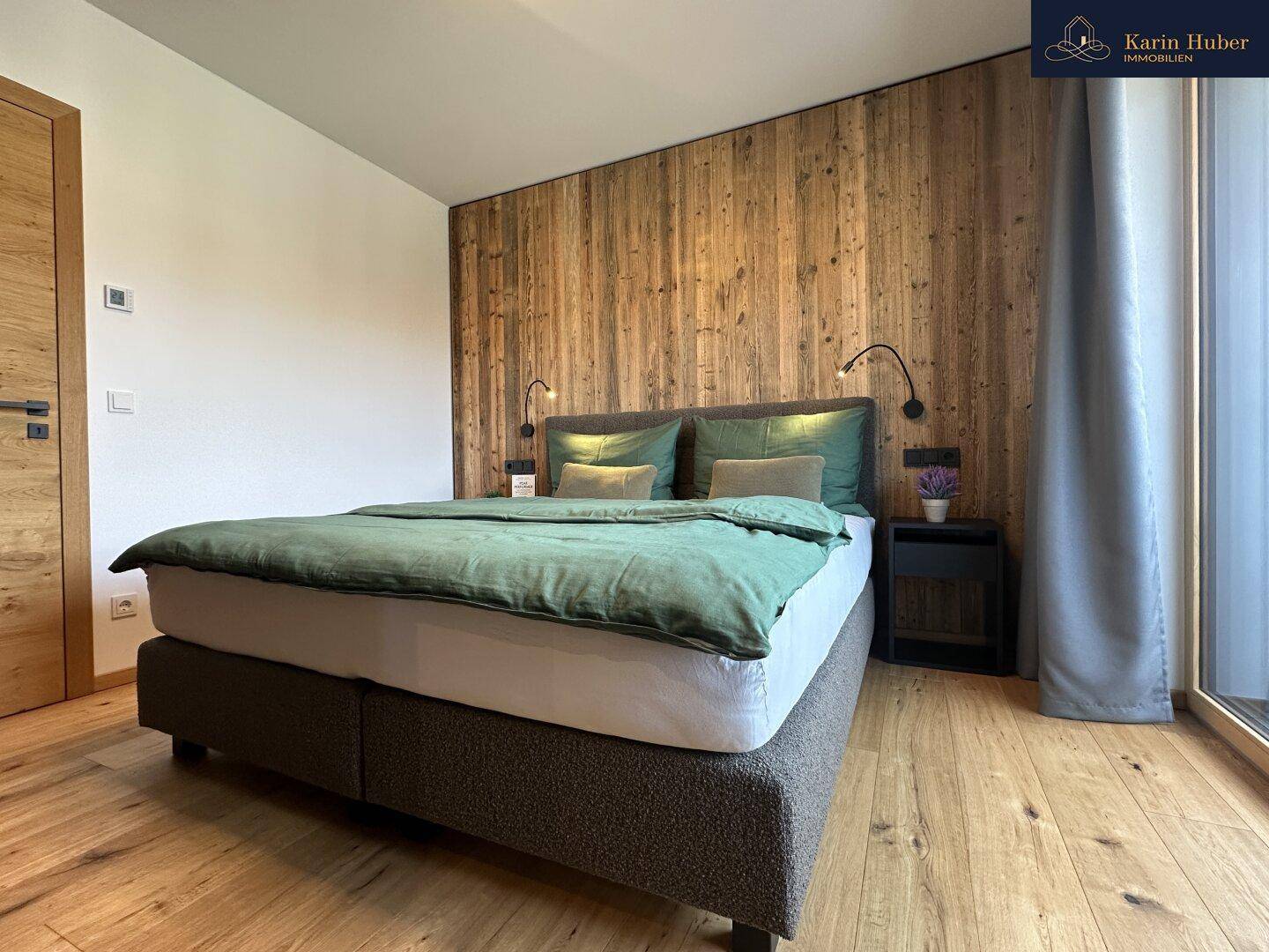Gemütliches Schlafzimmer mit Holzwand, großem Bett und Zugang zu einem Balkon oder Terrasse.