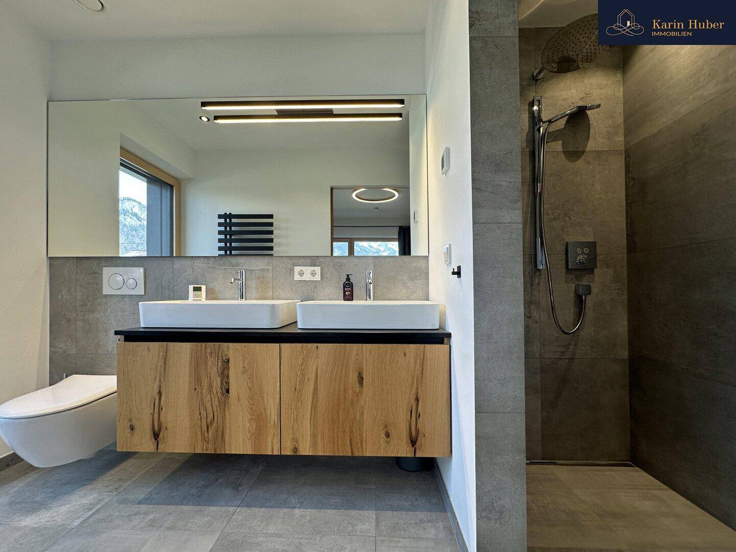 Geräumiges Badezimmer mit Doppelwaschbecken, großer Regendusche und Bergblick durch das Fenster.