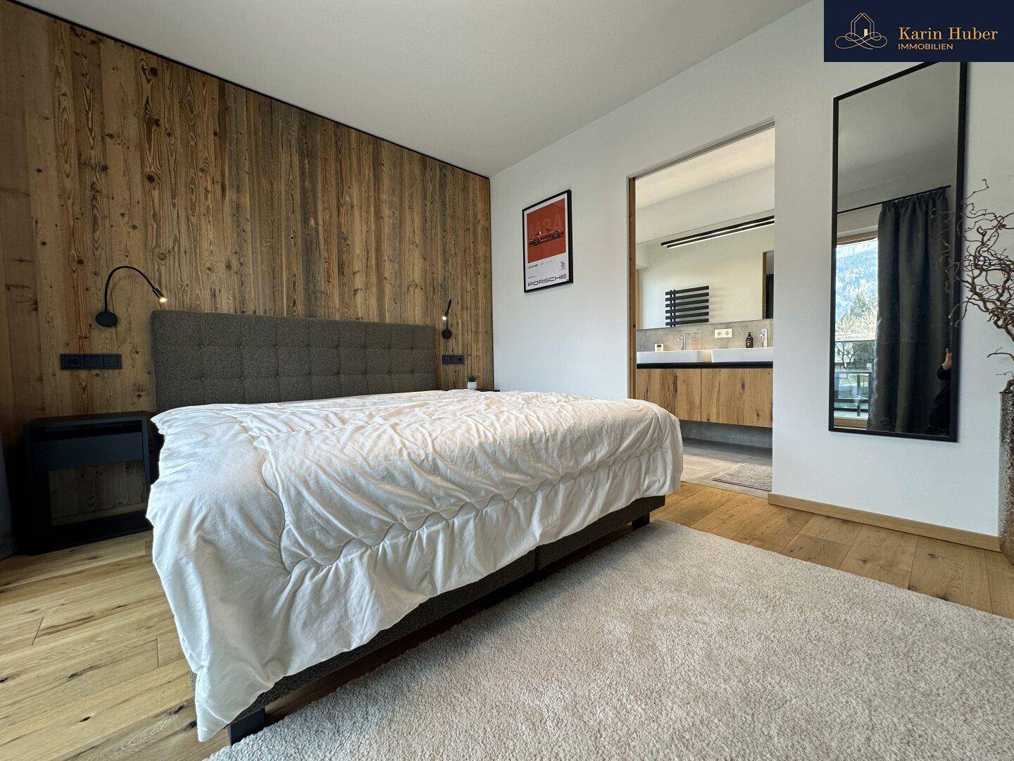 Schlafzimmer mit großem Bett, Holzboden und direktem Zugang zu einem modernen Badezimmer.