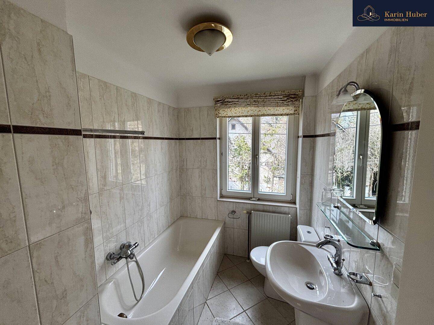 Helles Badezimmer mit Badewanne, Waschbecken, WC und Fenster für natürliche Belüftung.
