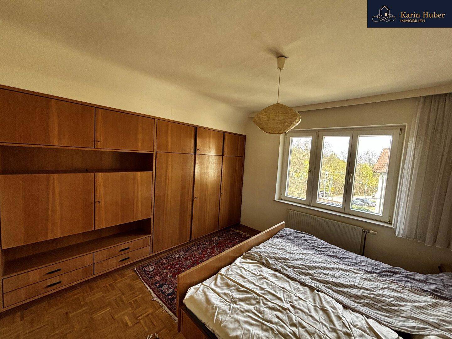 Gemütliches Schlafzimmer mit großem Bett, Holzschränken und Blick ins Grüne.