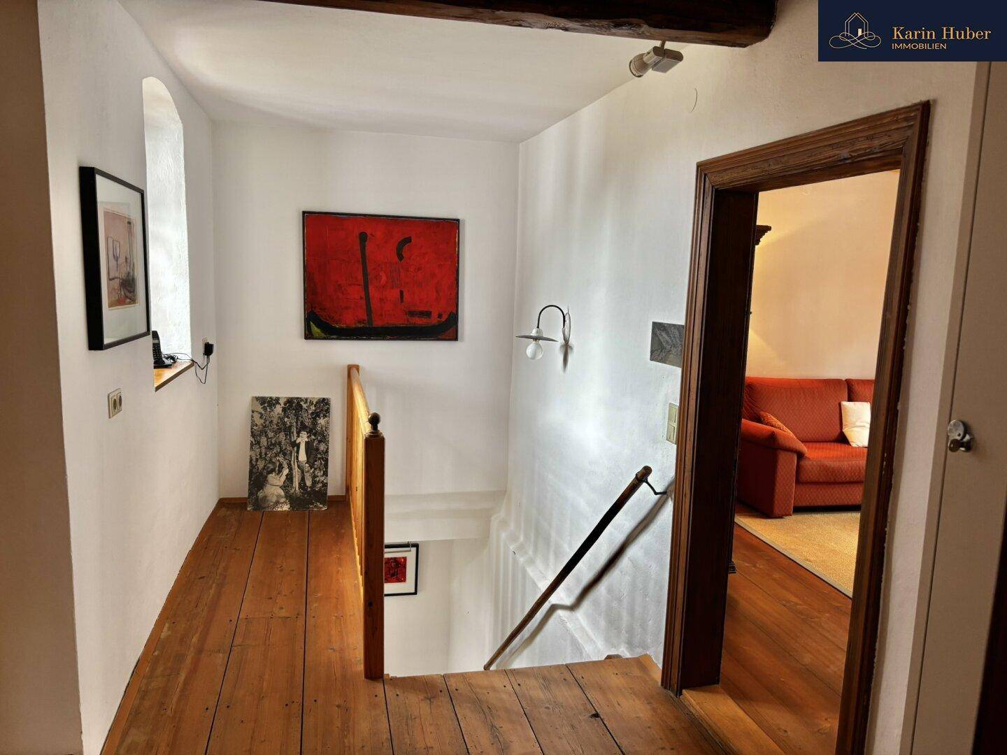 Flur mit Holzboden und sichtbaren Holzbalken, der zu weiteren Räumen und einer Treppe führt.