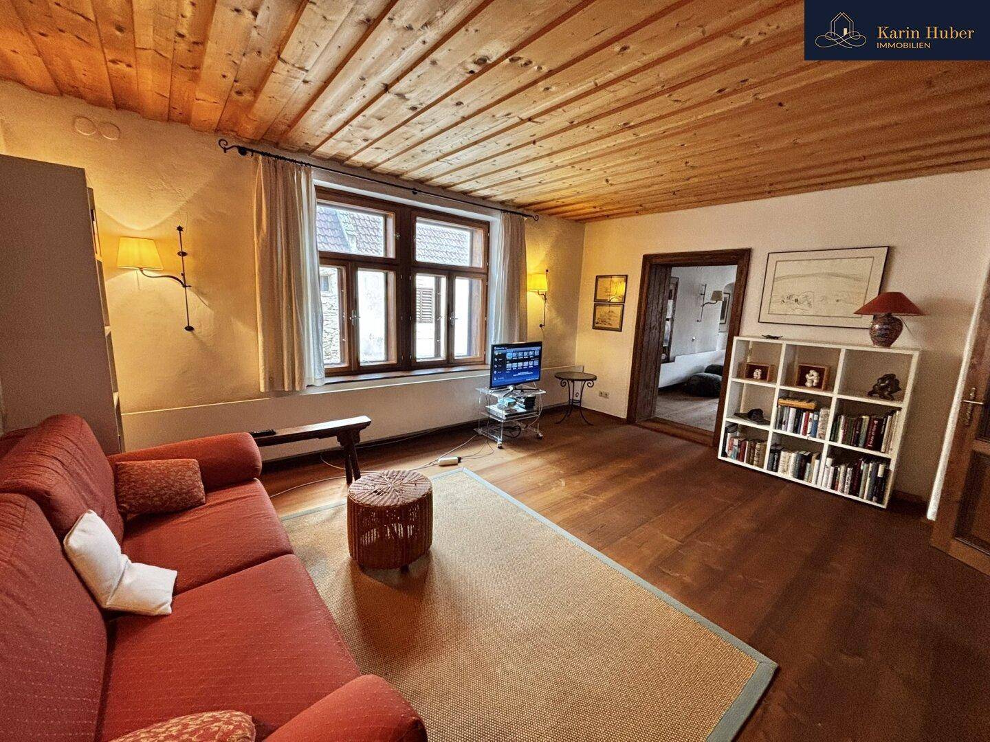 Geräumiges Wohnzimmer mit Holzbalkendecke, Holzboden und einem roten Sofa.