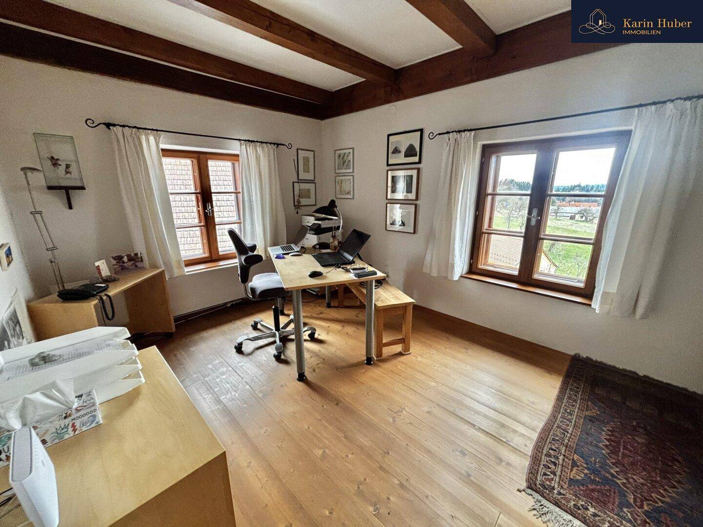 Helles Arbeitszimmer mit Holzboden, zwei Fenstern und einem Schreibtisch.