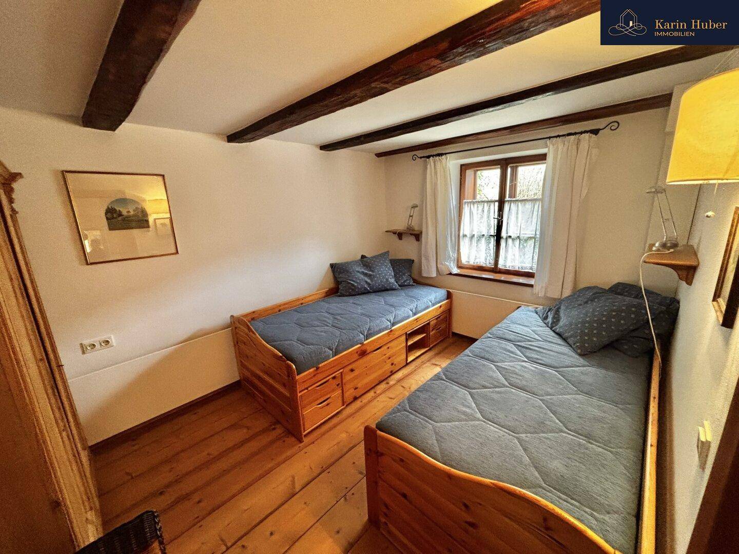 Gemütliches Schlafzimmer mit zwei Einzelbetten, Holzboden und einem Fenster.
