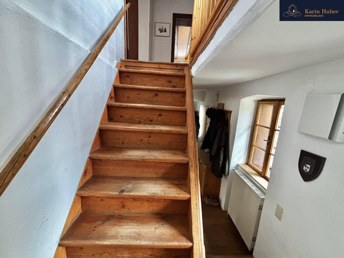 Holztreppe führt in den oberen Stock, mit weiß getünchten Wänden und einem Fenster.