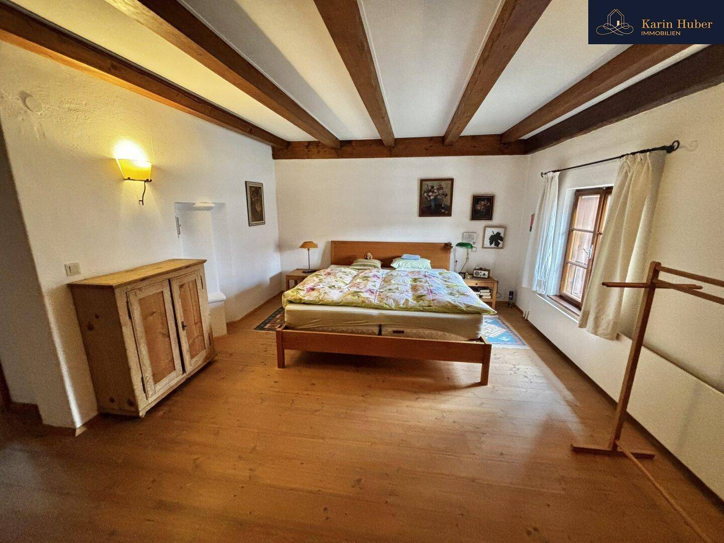 Geräumiges Schlafzimmer mit Doppelbett, Holzboden und sichtbaren Holzbalken an der Decke.