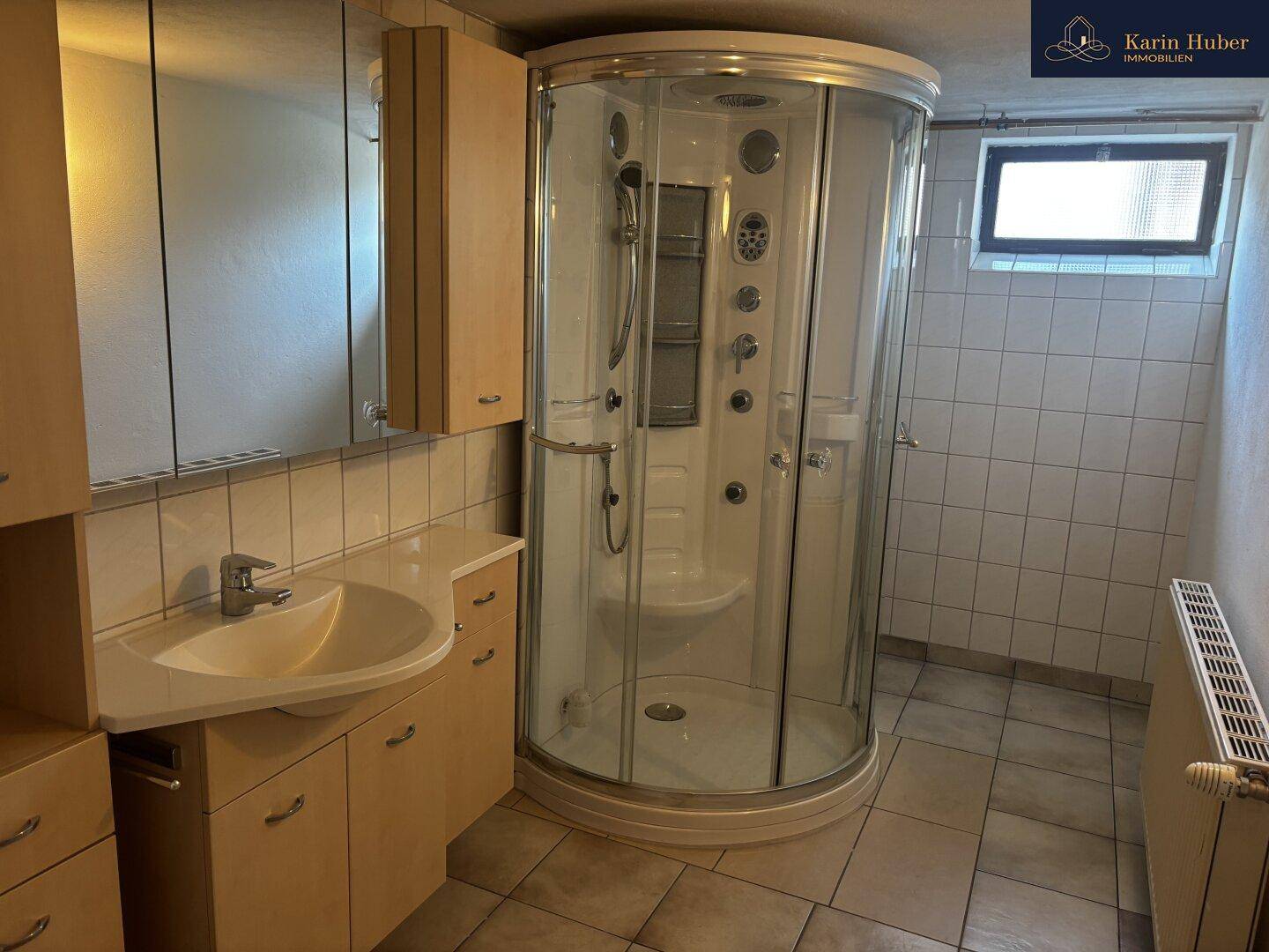 Badezimmer mit Duschkabine, Einzelwaschbecken und Fliesenboden im Untergeschoss.