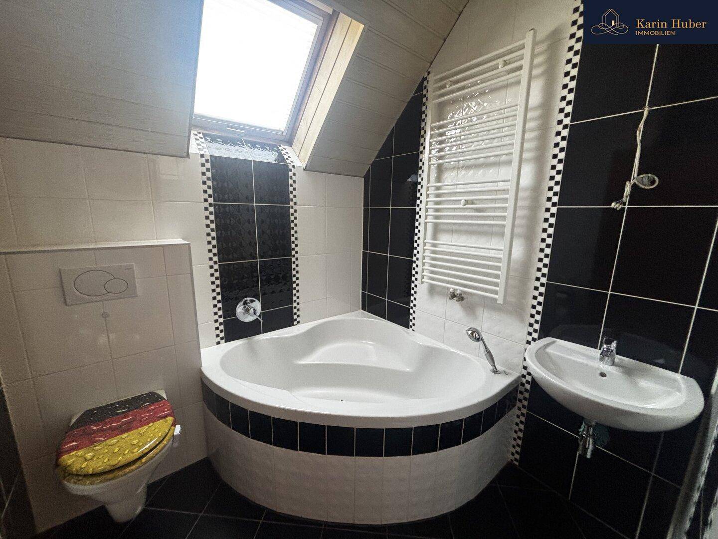 Badezimmer im Dachgeschoss mit Eckbadewanne, Dachfenster und Heizkörper.