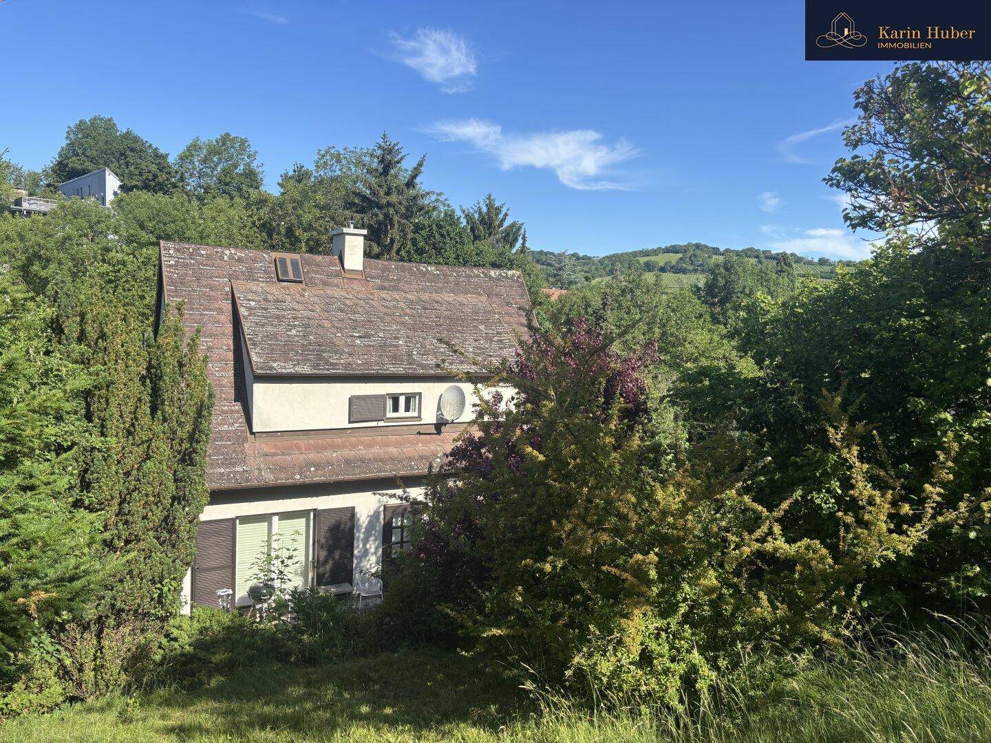 Charmantes Haus eingebettet in eine grüne Hügellandschaft unter strahlend blauem Himmel.