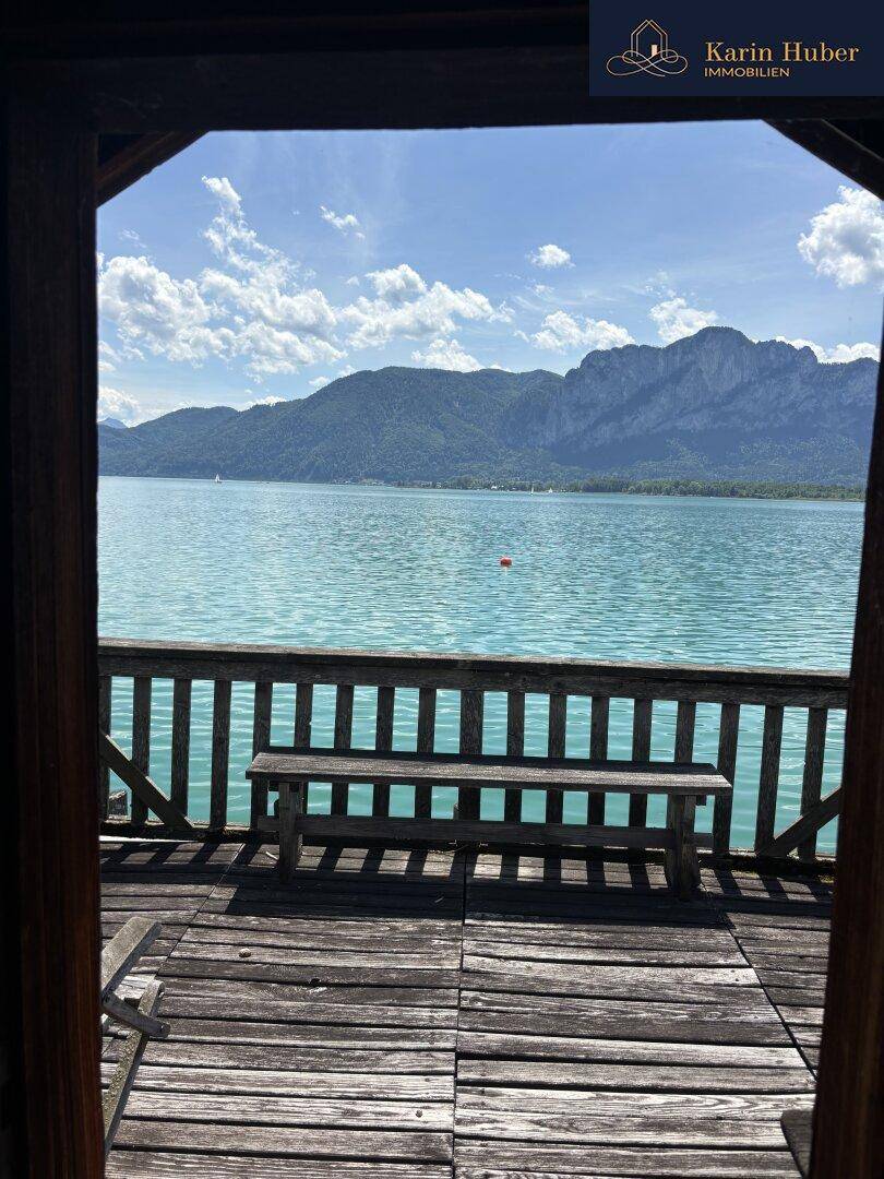 Blick von einer überdachten Holzterrasse auf den türkisblauen See und die majestätischen Berge.