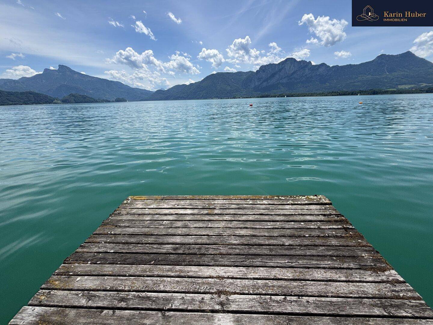 Hölzerner Steg ragt in das klare, türkisfarbene Seewasser mit weitem Blick auf die Berglandschaft.