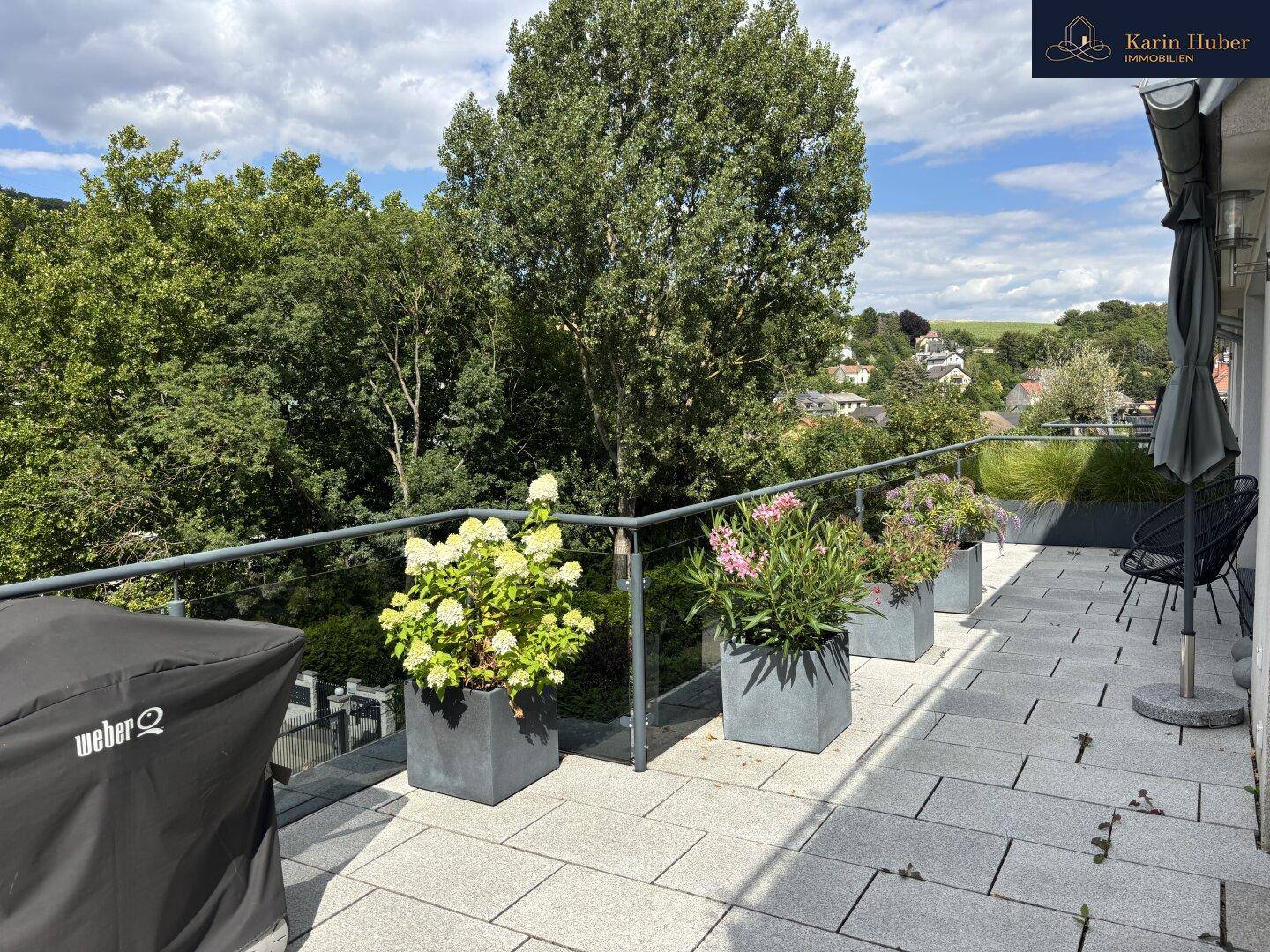Helle Terrasse mit Topfpflanzen und Grill, mit weitem Blick auf die grüne Landschaft.