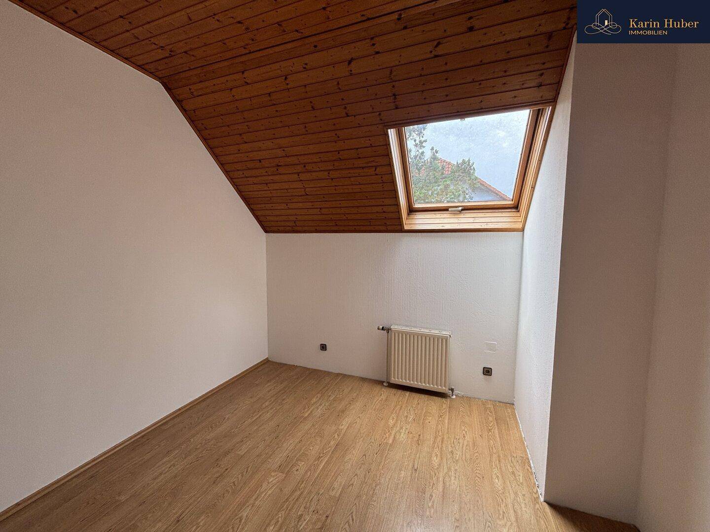 Helles Zimmer im Dachgeschoss mit schräger Decke, Laminatboden und Dachfenster.