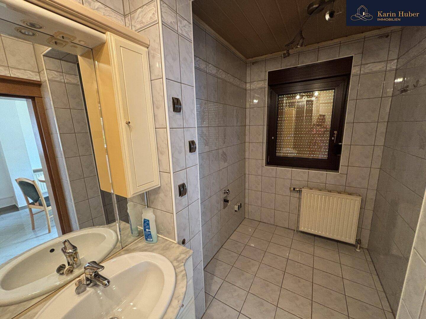 Badezimmer mit Doppelwaschbecken, Spiegelschrank und Fliesenboden.