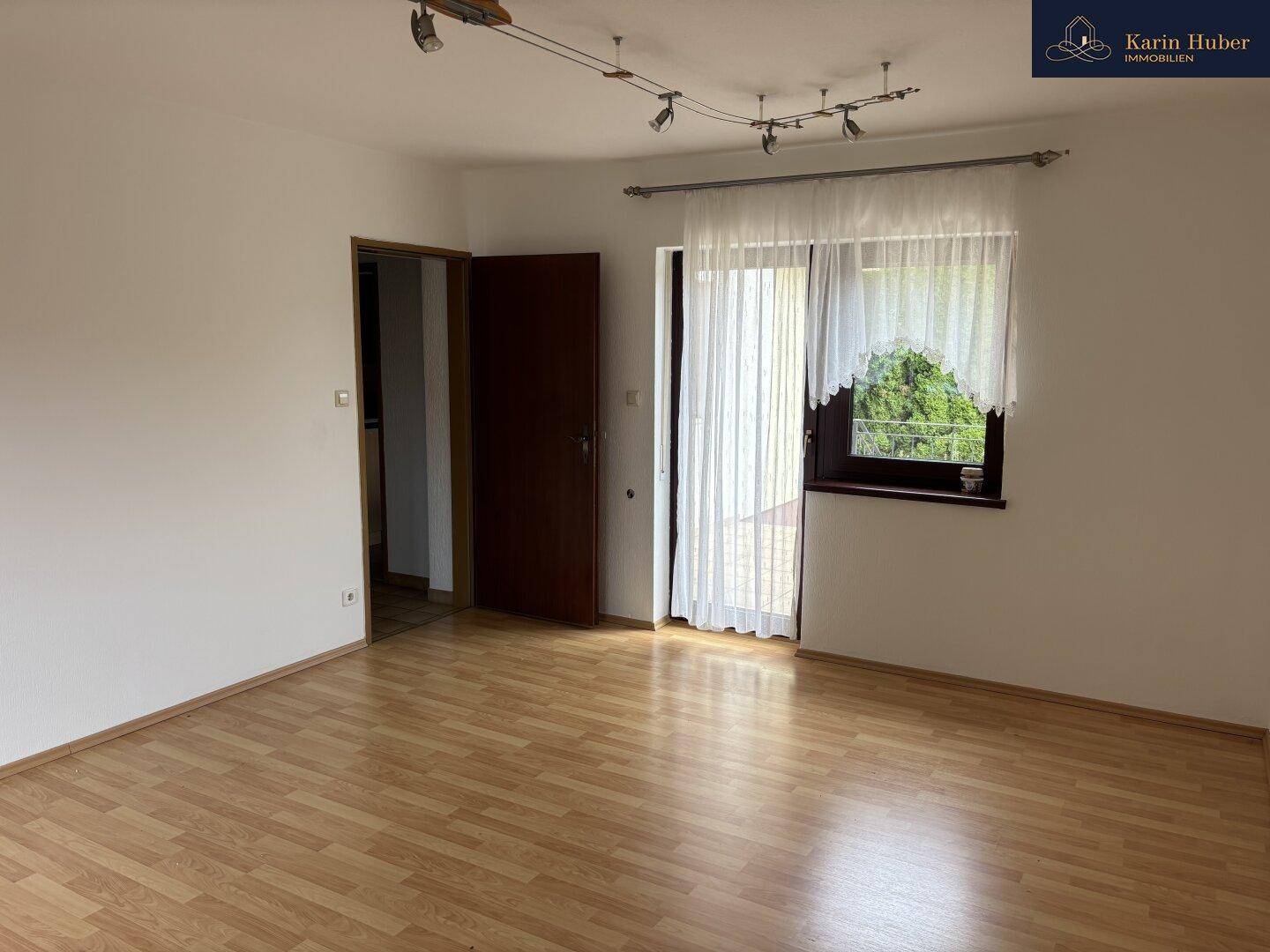 Geräumiges Wohnzimmer mit Laminatboden und großem Fenster, das viel Tageslicht hereinlässt.