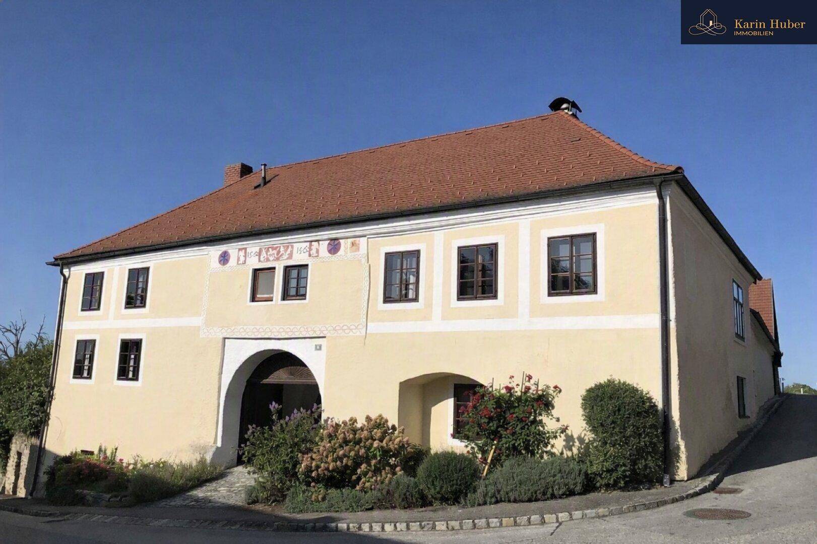 Traditionelles Gebäude mit hellgelber Fassade, roten Ziegeldächern und einem großen Torbogen.