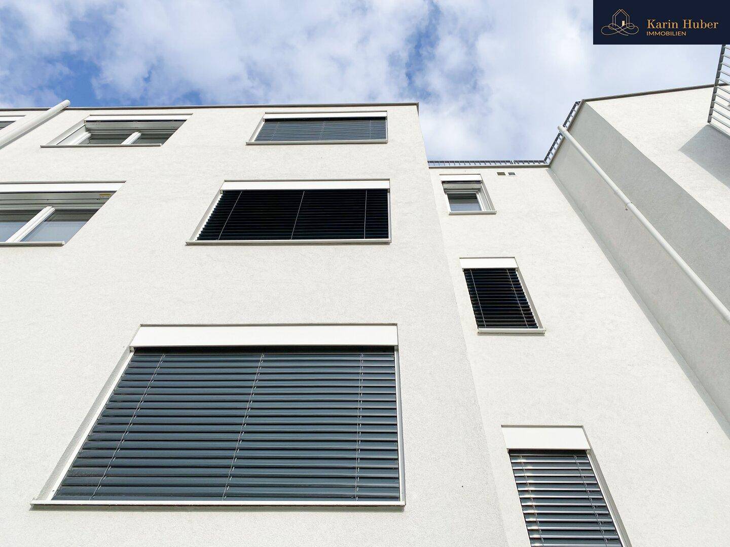 Fassade eines modernen Gebäudes mit großen Fenstern und außenliegenden Jalousien.