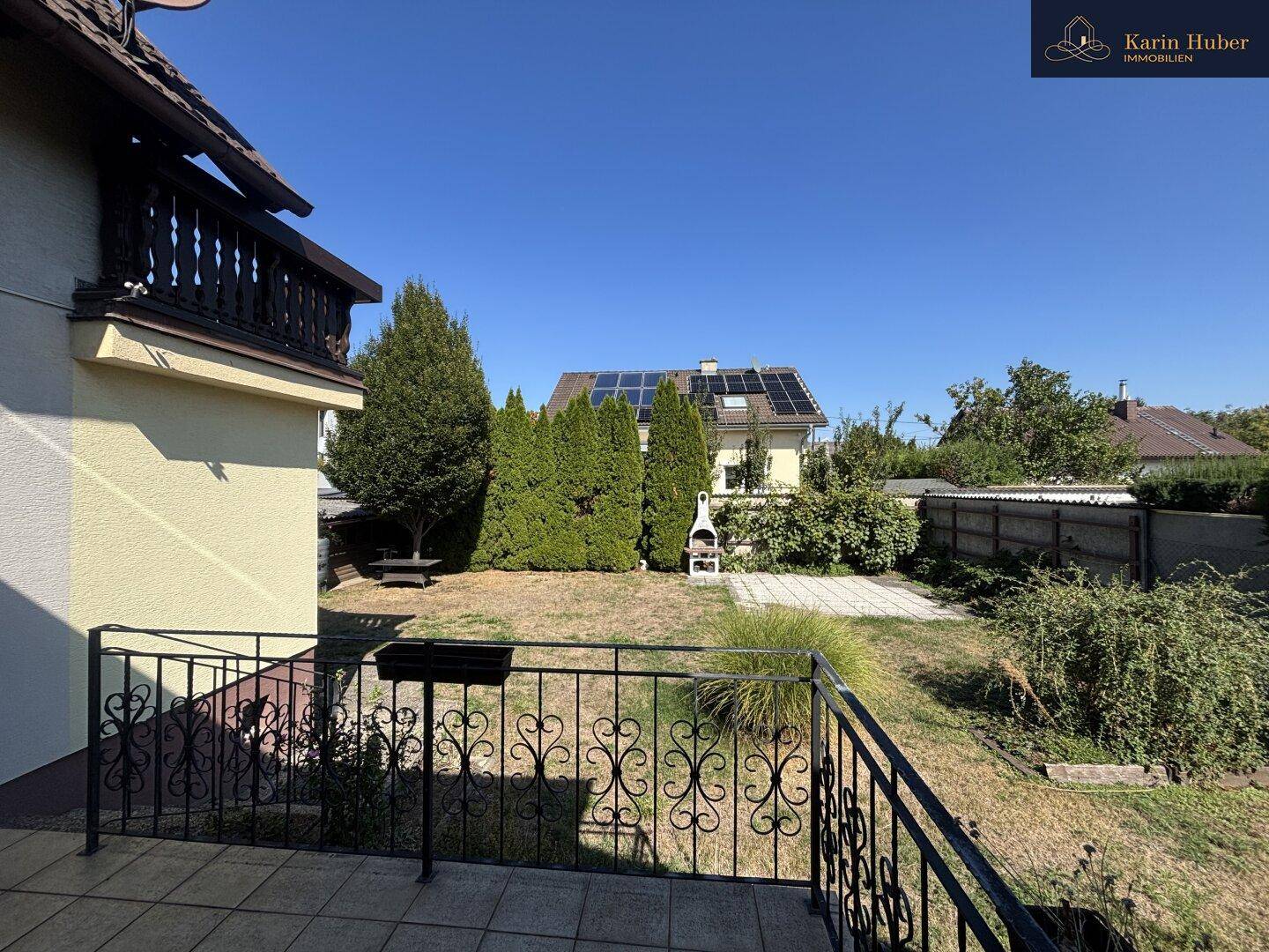 Hinterhof mit Rasenfläche, Grillplatz und Blick auf Nachbarhäuser mit Solaranlagen.