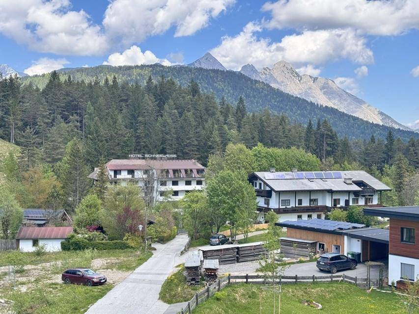 Panoramablick auf das Hotel und umliegende Häuser mit majestätischen Bergen im Hintergrund unter blauem Himmel.