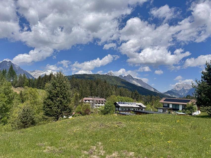 Ausgedehnte grüne Hügellandschaft mit vereinzelten Gebäuden und einem klaren Blick auf die umliegenden Berge.