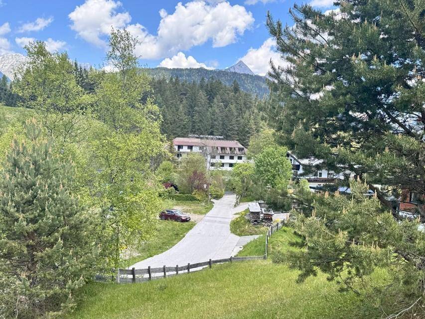 Weitläufige Landschaft mit Hotel, weiteren Gebäuden und beeindruckendem Bergpanorama unter blauem Himmel.