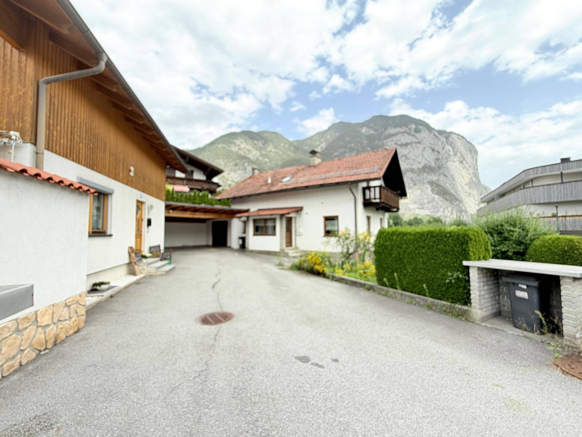 Zufahrt zum Haus mit Carport und Blick auf die umliegende Berglandschaft unter bewölktem Himmel.