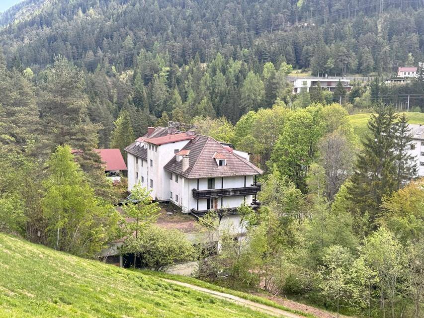 Rückansicht des Hotels mit traditionellem Dach und Balkonen, eingebettet in eine grüne Hügellandschaft.