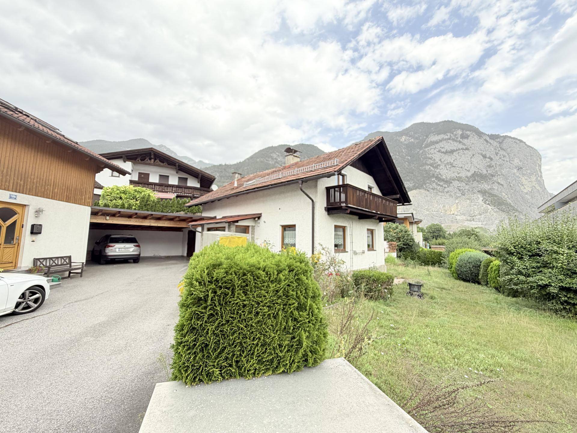 Haus mit Zufahrt, Carport und Bergblick, umgeben von grünen Büschen.