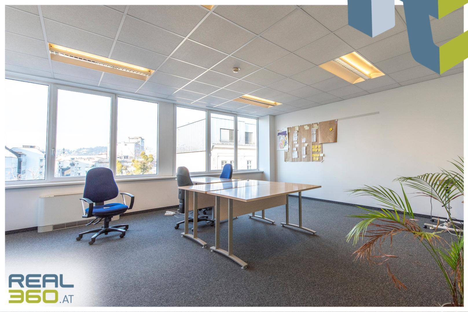 Helles Büro mit zwei Schreibtischen, Bürostühlen und großen Fenstern, die eine weite Aussicht ermöglichen.