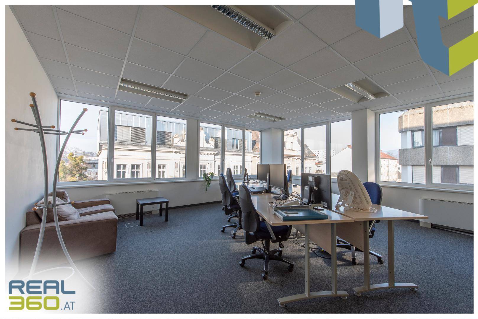 Büro mit mehreren Arbeitsplätzen, großen Fenstern und Blick auf die umliegenden Gebäude.