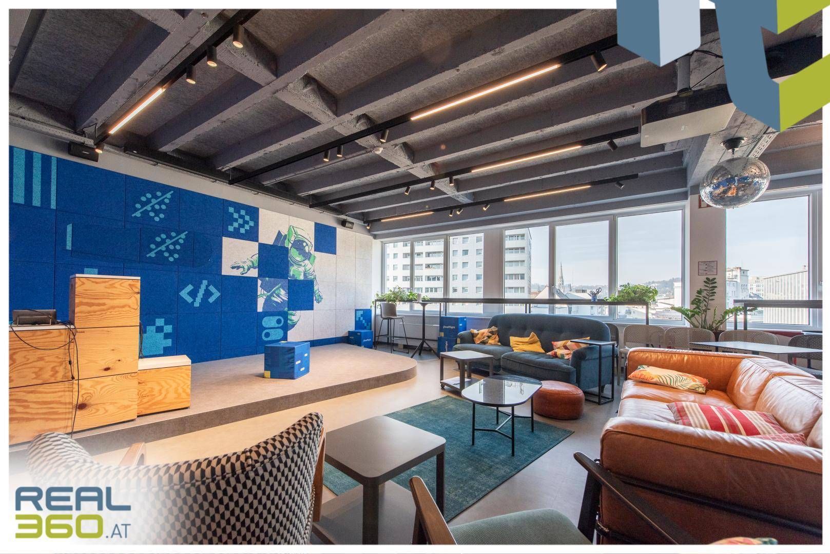 Entspannter Loungebereich mit Sofas, Couchtischen und einer Bühne, ideal für Präsentationen oder Events.