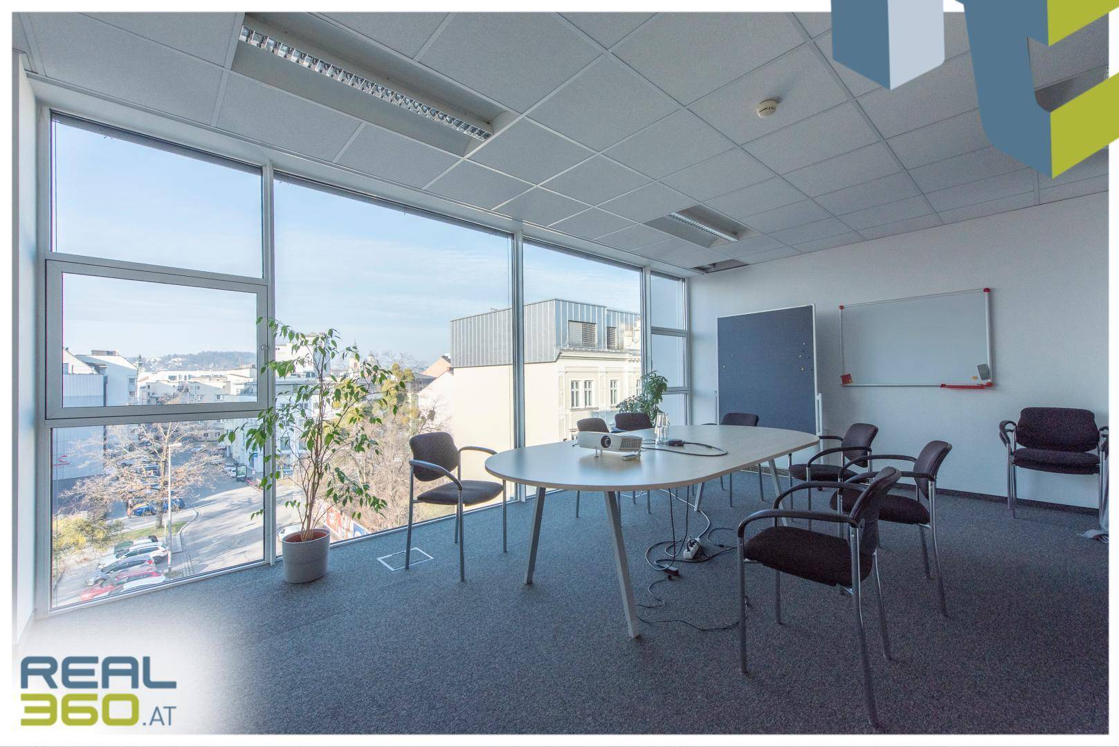 Konferenzraum mit großem ovalen Tisch, vielen Stühlen und raumhohen Fenstern mit Stadtblick.