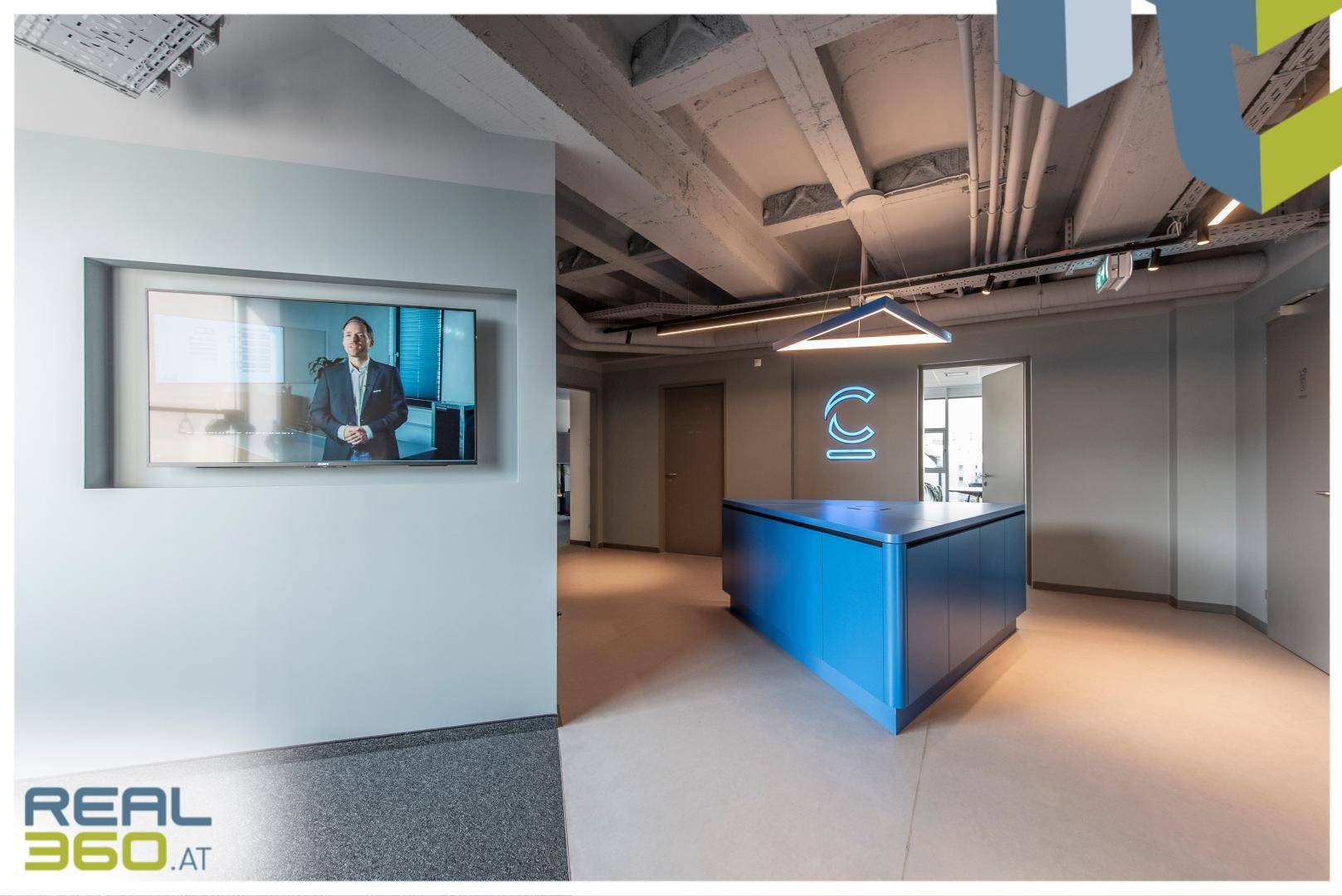 Moderner Empfangsbereich mit blauer Theke, Bildschirm und freiliegenden Deckenrohren im Industriedesign.