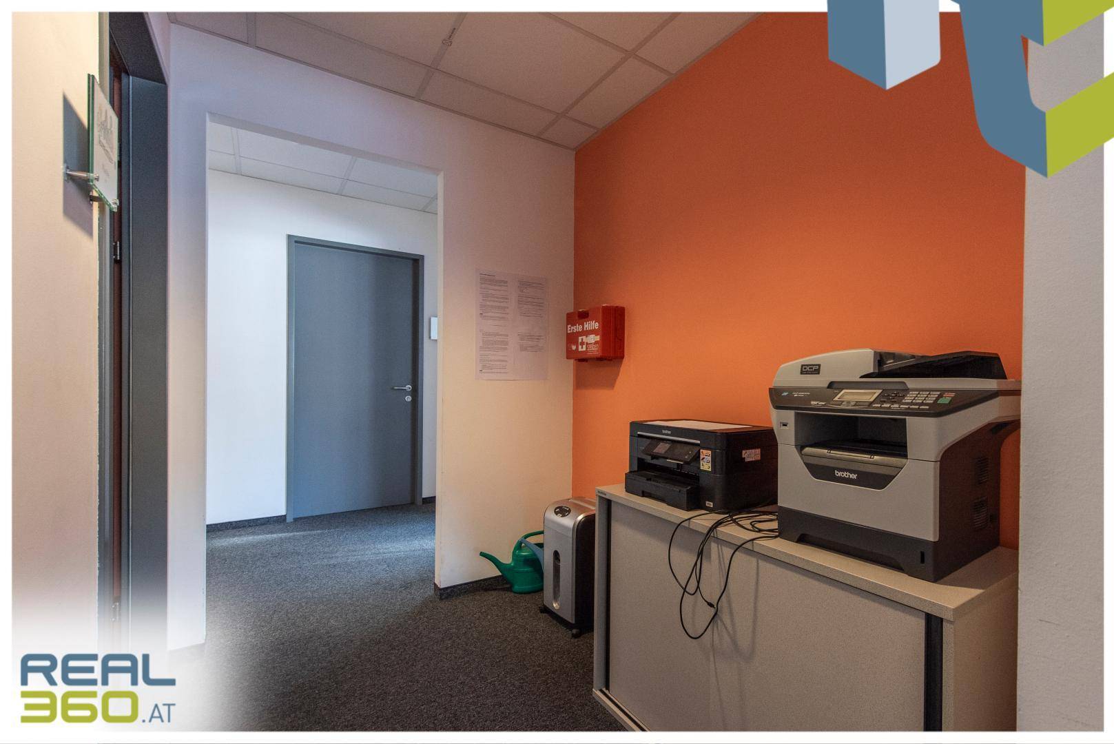 Bürogang mit orangefarbener Akzentwand, Drucker und Feuerlöscher, funktional und hell.
