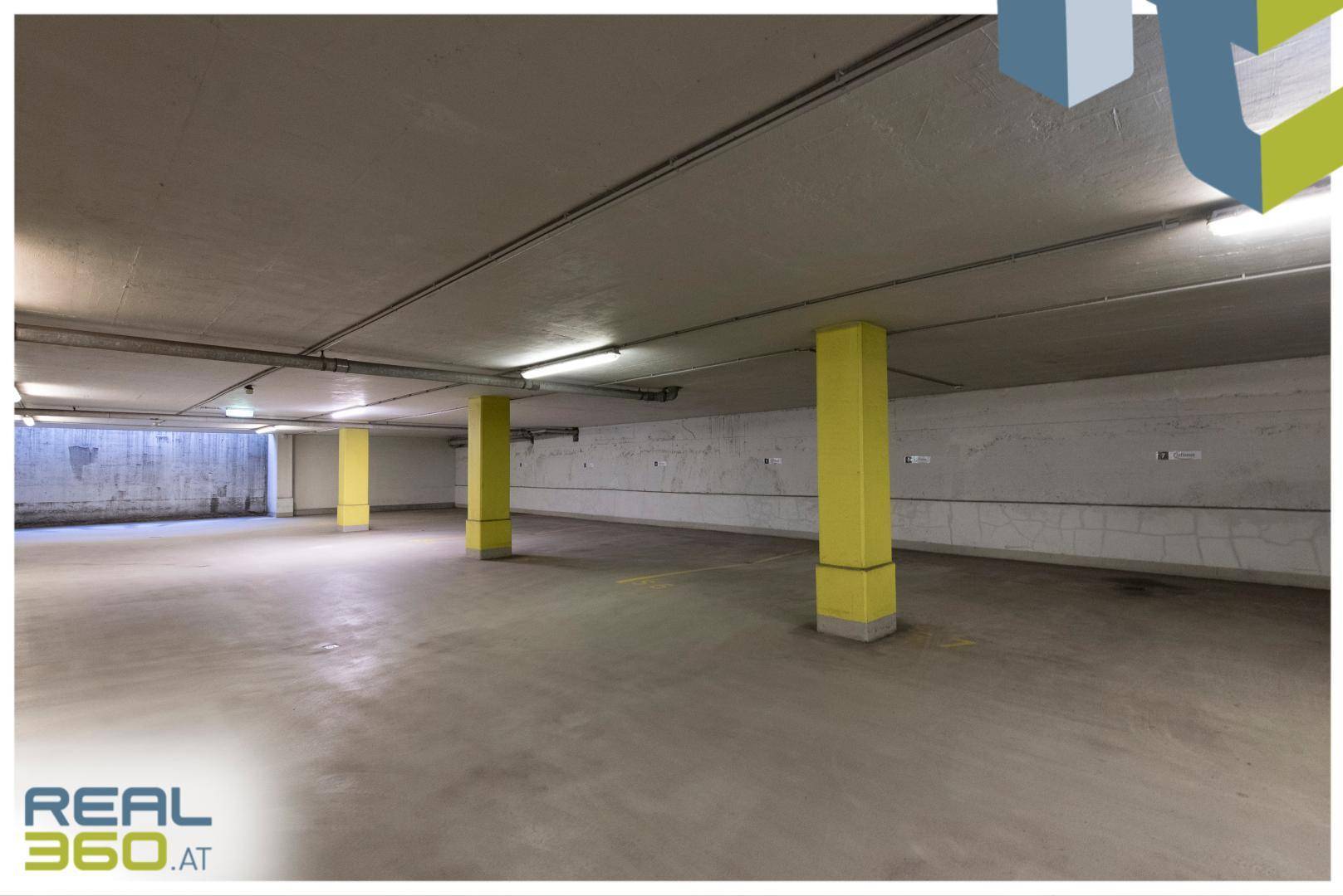 Geräumige Tiefgarage mit gelben Säulen und Betonboden, bietet ausreichend Parkmöglichkeiten.